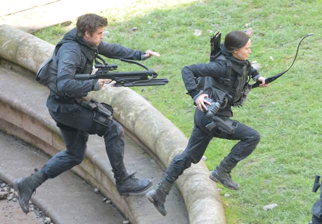 Liam Hemsworth et Jennifer Lawrence en tenues de combat, armés d'un arc et d'une arbalète