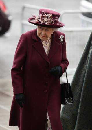 La reine Elizabeth II tout de bordeaux vêtue et d'un chapeau fleuri