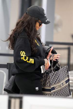 Rihanna voyage en tenue confortable, sweat noir et caba Dior brodé à son nom à la main.