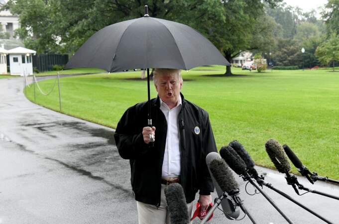 Donald Trump sous son parapluie répondant aux journalistes avant son embarquement