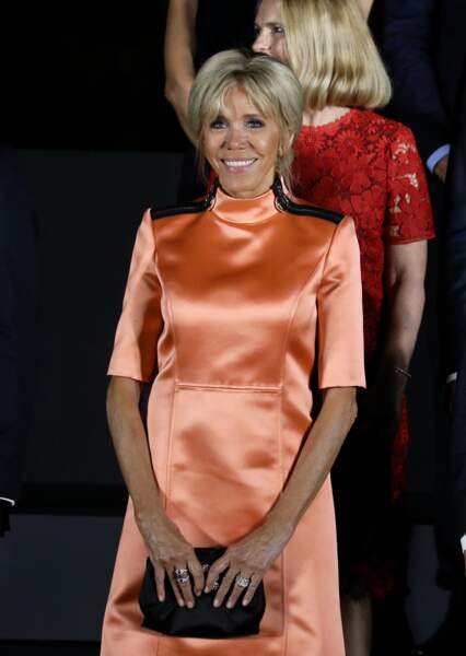 Cheveux attachés et relevés en chignon, Brigitte Macron très souriante en robe courte en satin