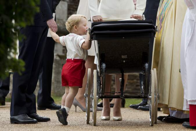 Le prince George observe sa petite soeur, Charlotte, lors de son baptême à Sandringham le 5 juillet 2015