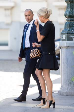 A son bras, un sac à bandoulière chaîne signé Louis Vuitton, en cuir damier noir et camel.