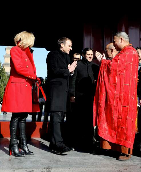 Brigitte Macron une femme tout en rouge et noir avec un manteau d'officier Balmain et un sac Louboutin