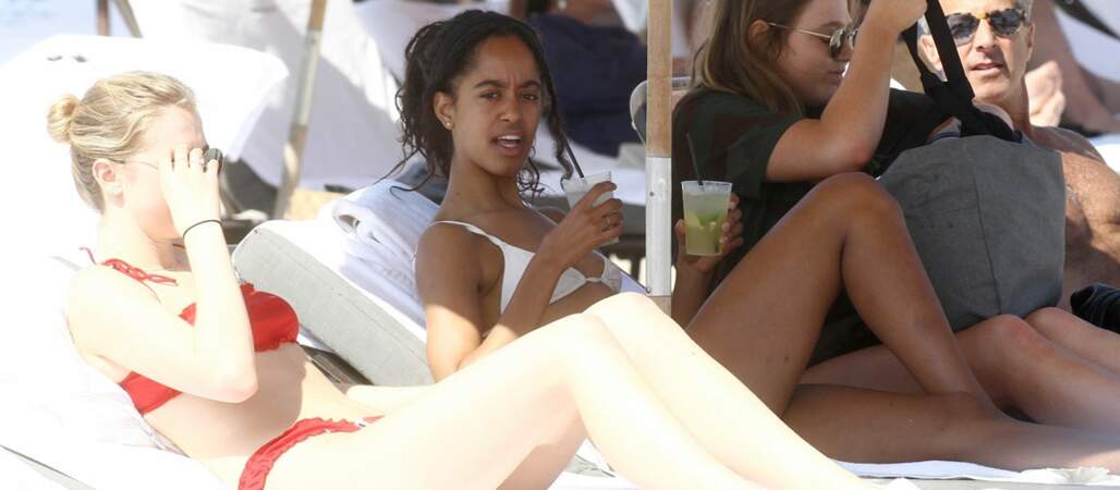En maillot de bain deux-pièces blanc sur la plage, Malia Obama se détend, un cocktail à la main.