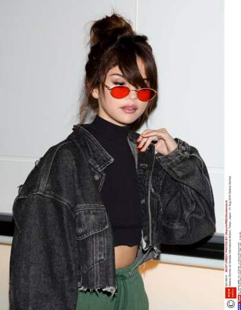 Plongée 70's pour Selena Gomez qui réhabilite la longue frange décalée sur son chignon bun, avec lunettes rondes
