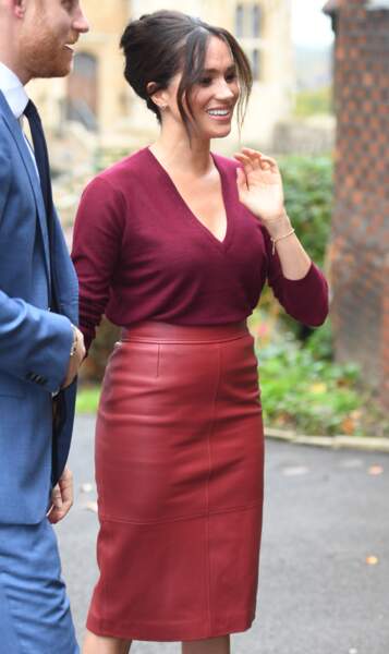 Meghan Markle femme glamour en jupe taille haute en cuir rouge bordeaux assorti à son pull col v.