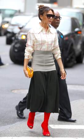 Victoria Beckham a revêtu une jupe midi bicolore et légèrement plissée portée avec des bottes chaussettes en cuir rouge flashy.