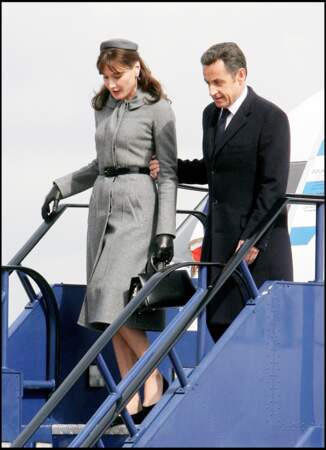 Carla Bruni fait un sans faute à son arrivée à l'aéroport d'Heathrow au Royaume-Uni dans un style à la Jackie Kennedy avec un bibi assorti à son manteau gris ceinturé. A ses côtés, Nicolas Sarkozy apparaît fier.