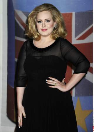 2012 : Adele pendant les Brit Awards 2012 à l'Arena de Londres. Niveau look, Adele aime travailler le total look noir, serré à la taille. Elle a changé de couleur de cheveux, mise sur le volume et un maquillage plus prononcé.