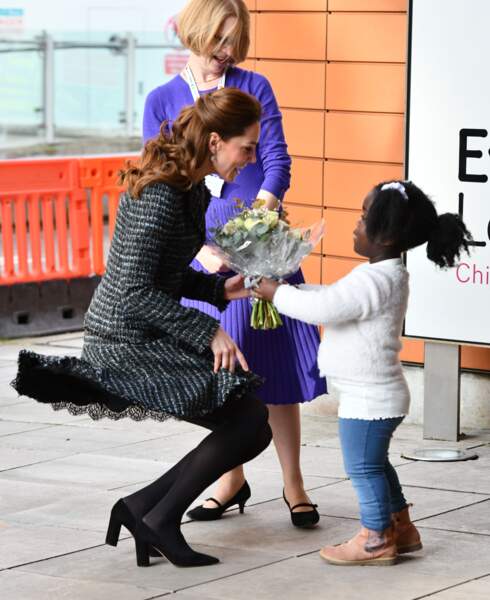 Kate Middleton maitrise sa jupe en tweed malgré le vent pour recevoir le bouquet offert par une des petites filles de l'hôpital.