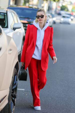Hailey Baldwin Bieber associe un costume rouge chic et un sweat à capuche gris pour sortir.