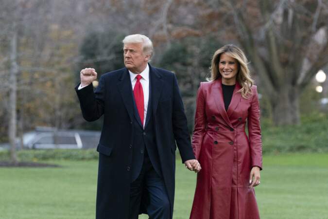Melania Trump souriante, vêtue avec un long manteau en cuir rouge, au côté de son mari.