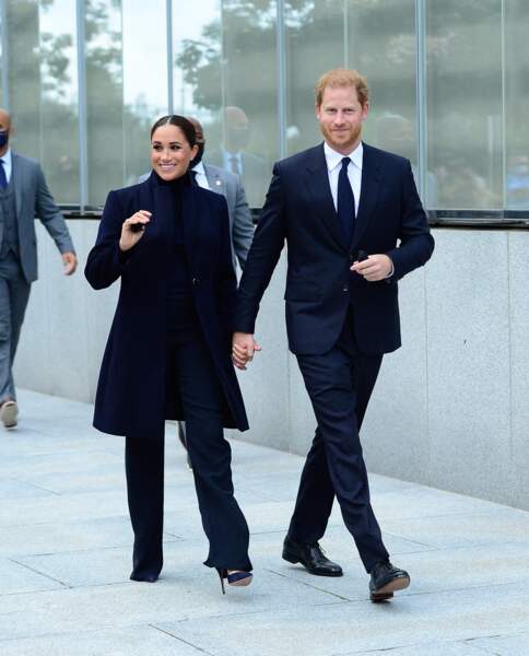 Meghan Markle en pantalon flare et manteau long et le prince Harry en costume, cravate et chemise blanche