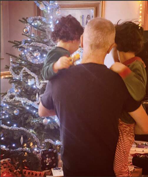 Samuel Etienne touchant avec ses deux enfants dans les bras devant le sapin de Noël.