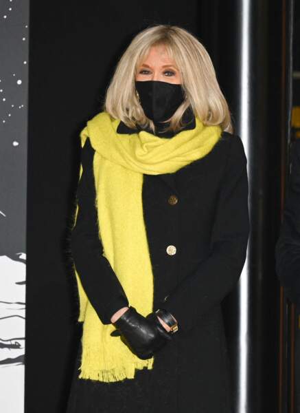 Brigitte Macron en manteau, masque et gants noirs assortis et écharpe jaune.