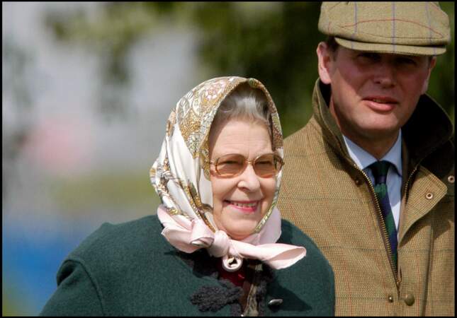 Lunettes de soleil et carré de soie noué sur la tête, la reine Elizabeth II a fait de ce combo sa propre signature, lors du salon du cheval à Windsor, le 13 mai 2005.