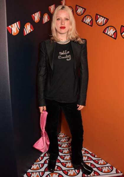 Harriet Verney rajoute une touche flashy à son total look noir : elle tient un sac rose fuchsia à la soirée de lancement de la collaboration Michael Kors X Ellesse, à Londres. Le 4 mai 2022.