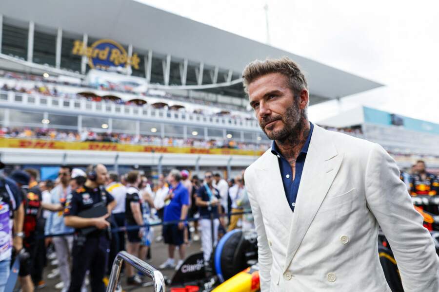 David Beckham en veste de costume blanche qu'il boutonne lors du Grand Prix de Formule 1 de Miami, le 8 mai 2022.