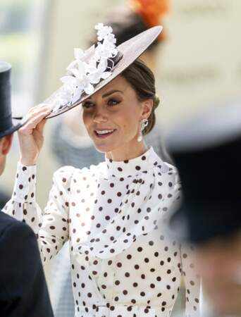 Kate Middleton coiffée d'un chignon dévoilant des perles à ses oreilles avec un chapeau tissé aux détails floraux en cascade.