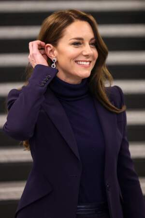 Lâchés au vent, Kate Middleton tente de replacer ses cheveux derrière l'oreille. Une façon de dévoiler ses luxueux bijoux le 30 novembre 2022