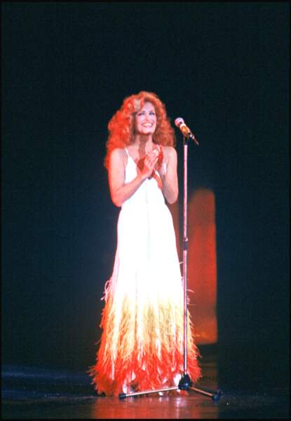 Dalida sublime dans une longue robe sertie de plumes colorées pour une représentation sur la scène du Palais des Sports, le 9 janvier 1980