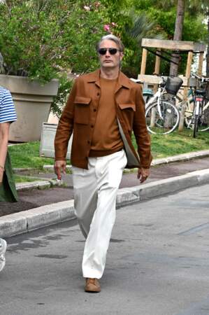 Mads Mikkelsen sur la Croisette en veste et tricot bruns et pantalon blanc, le 17 mai 2023 pour le 76e Festival de Cannes 
