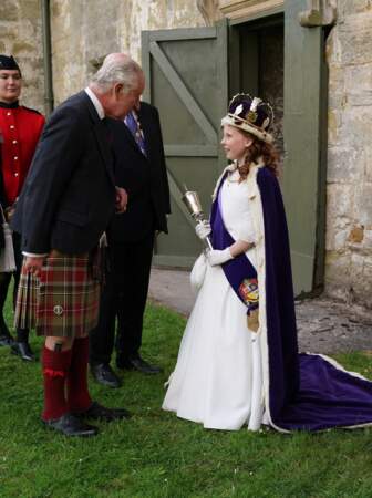 Le roi Charles III est accueilli par Lexi Scotland vêtue de sa robe de cérémonie et une couronne, le 3 juillet 2023. 