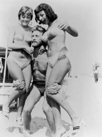 Kirk Douglas montre la force de ses bras en slip de bain sur la plage du Lido, en 1953.