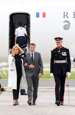 Brigitte Macron porte un long manteau en tweed blanc, un pull col lavallière, un slim noir, une paire d'escarpins 