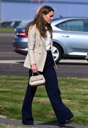 Kate Middleton porte un pantalon large bleu, une veste de blazer de la marque Reiss et un sac à mains Tusting