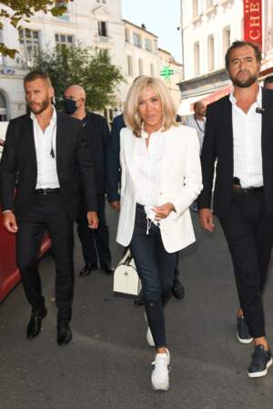 Brigitte Macron  : tenue casual chic entre sac griffé, veste blanche, pantalon slim et sneakers blanches le 25 août 2021