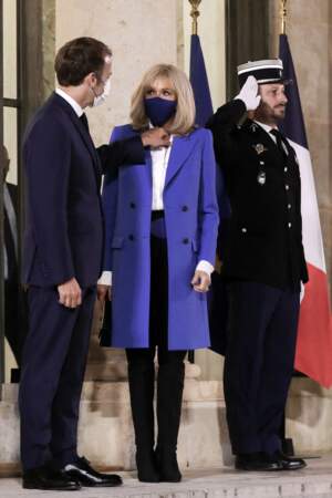Brigitte Macron chic en veste longue, chemise blanche et pantalon noir