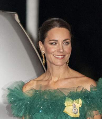 Kate associe sa tenue à des bijoux prêtés par la reine, et sur laquelle elle accroche son insigne royale fétiche : un nœud jaune à l'effigie de la reine. Le 23 mars 2022. 