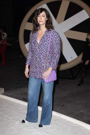 Anna Mouglalis concorde son jean flare à une blouse en tweed violette et rose assortie d'un sac Chanel de cette même couleur flashy. 