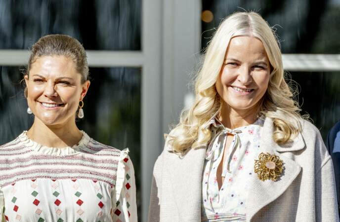 La princesse Mette-Marit de Norvège accroche une imposante broche dorée à son manteau By Malina en Suède, le 2 mai 2022.  