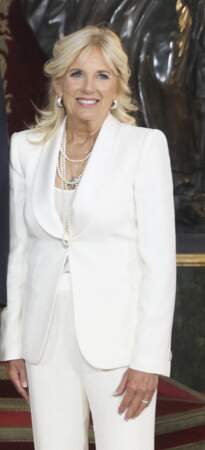 Jill Biden boutonne sa veste de blazer blanc qu'elle porte avec une accumulation de colliers en perles, le 28 juin 2022. 