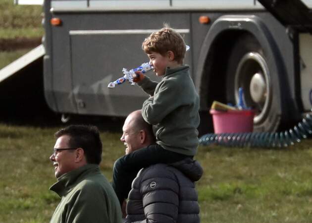 À six ans, le prince George sur les épaule de Mike Tindall, un joueur de rugby international anglais, lors d'un après-midi en famille en marge des courses hippiques de Burnham le 12 avril 2019 dans le Norfolk (Angleterre)