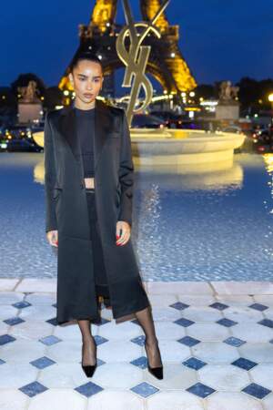Zoe Kravitz est glamour dans un ensemble top-jupe noir qu'elle recouvre d'un long manteau au défilé Saint Laurent lors de la Fashion week de Paris , le 27 septembre 2022.