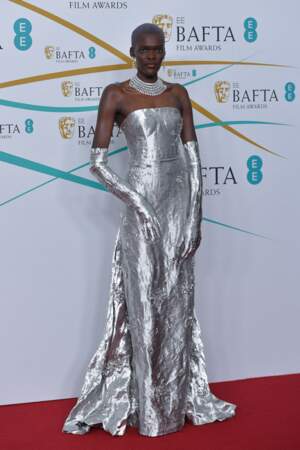 Sheila Atim arbore une robe bustier argentée avec de longs gants opéra ton sur ton de chez Prada aux Bafta 2023