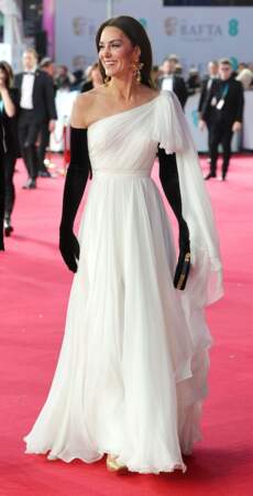 Kate Middleton porte une robe en mousseline blanche d’inspiration mariage, signé du créateur Alexander McQueen qu’elle avait déjà porté lors des BAFTA 2019. Pour accessoiriser son fourreau immaculé, l’épouse du prince William portait de longs gants opéra en velours noir, assortis à la veste de son mari ainsi que des escarpins dorés de la marque Aquazzura. Côté bijoux, Kate Middleton arborait une paire de boucles d’oreille dorées accessibles de chez Zara au prix de 20€.