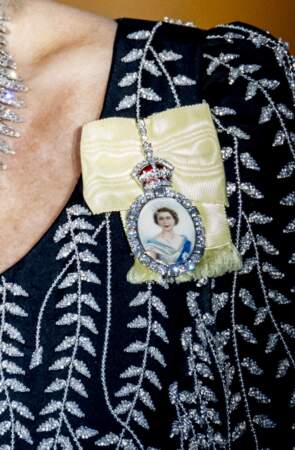 Le 29 mars 2023, Camilla Parker Bowles épingle sur sa toilette la médaille de la famille de la reine Elizabeth II : The Royal Family. Ce ruban de chartreuse jaune auréolé de diamants est décoré d’une miniature peinte en ivoire représentant la Reine Elizabeth.