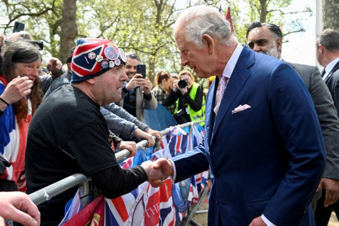 Charles III amusé, qui serre la main d'un sympathisant présent devant le palais de Buckingham, vendredi 5 mai 2023, à la veille de son couronnement.