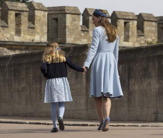 La princesse Charlotte porte deux fines tresses nouées derrière la tête sous un ruban bleu lors alors qu'elle quitte la chapelle Saint-Georges de Windsor avec sa mère le 17 avril 2022