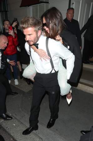 David Beckham porte sa femme Victoria Beckham sur son dos, à la sortie de la soirée de son 50ᵉ anniversaire au club Oswald's à Londres, le 20 avril 2024
